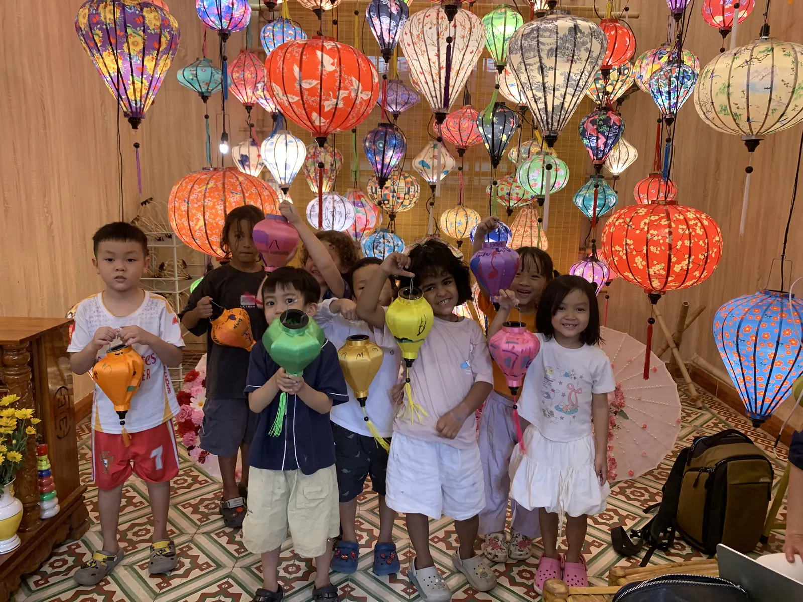 Primary students with the lanterns they made, under the lanterns of Hội An