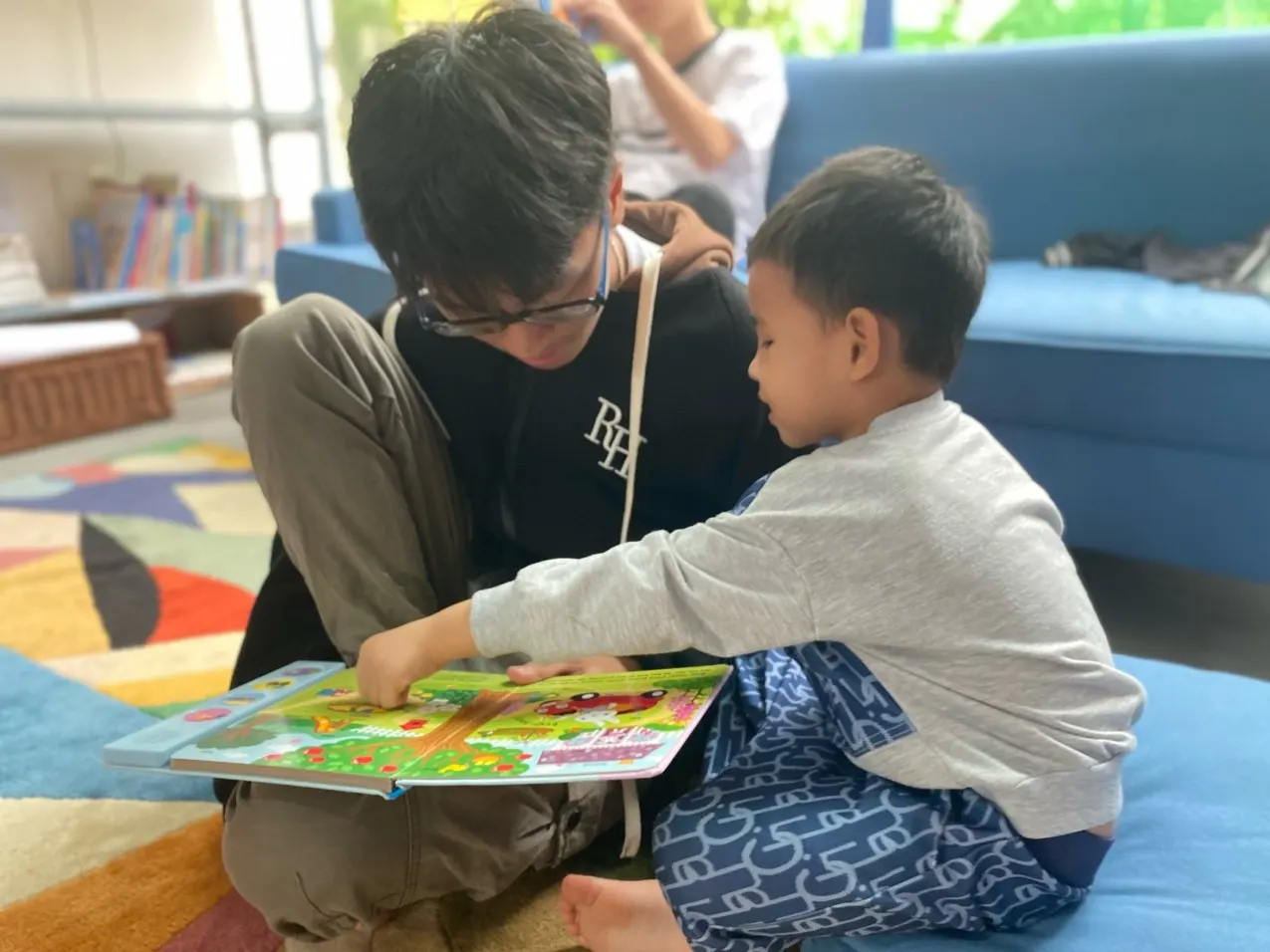 An Upper Secondary student sharing a book with a younger child on the classroom rug